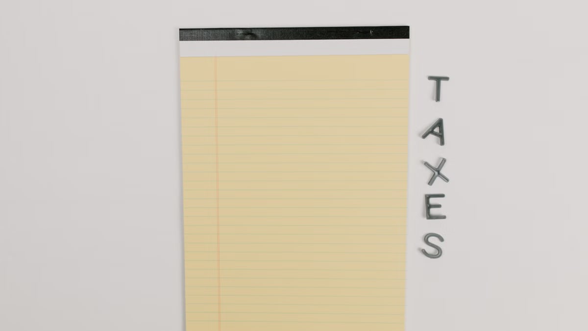 Close-up of a yellow legal pad and the word 'TAXES' on a white surface, ideal for finance themes.